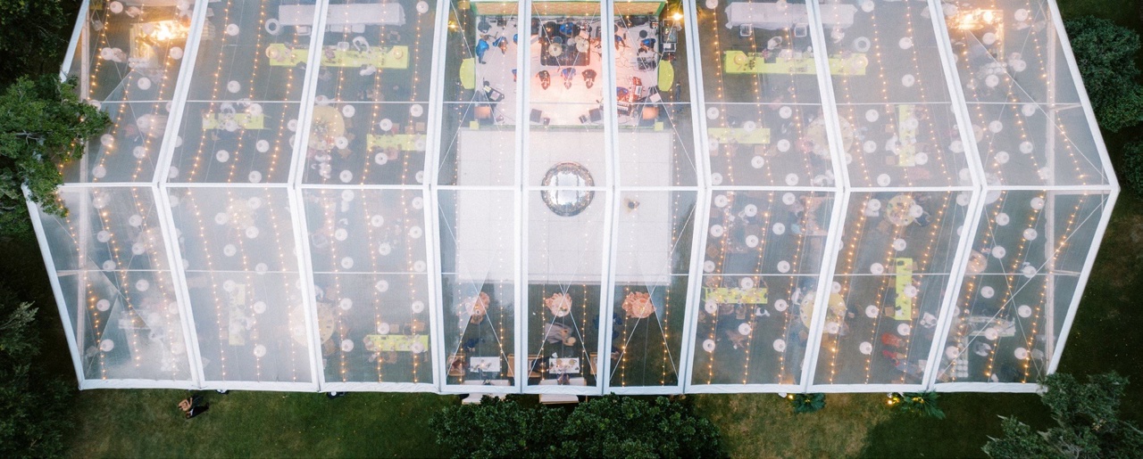 An aerial view of a lit TopTec clear-span event tent at dusk